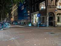 two bikes parked on the sidewalk next to some building by street lamps at night at night