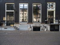 a very small apartment building with large windows and stone pathway outside a door on the street