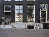 a very small apartment building with large windows and stone pathway outside a door on the street