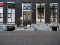 a very small apartment building with large windows and stone pathway outside a door on the street