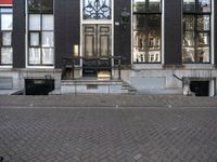 a very small apartment building with large windows and stone pathway outside a door on the street