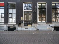 a very small apartment building with large windows and stone pathway outside a door on the street