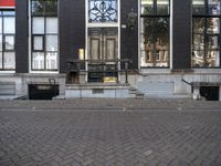 a very small apartment building with large windows and stone pathway outside a door on the street