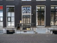 a very small apartment building with large windows and stone pathway outside a door on the street