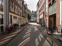 a narrow street with bicycles parked on the side of it next to tall buildings and people