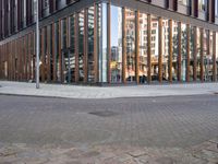 a brick street next to an office building with a wooden and glass facade and people walking down the sidewalk