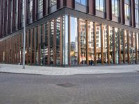 a brick street next to an office building with a wooden and glass facade and people walking down the sidewalk