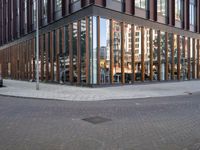 a brick street next to an office building with a wooden and glass facade and people walking down the sidewalk