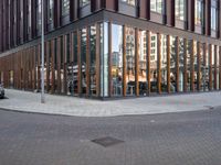 a brick street next to an office building with a wooden and glass facade and people walking down the sidewalk