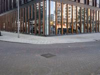 a brick street next to an office building with a wooden and glass facade and people walking down the sidewalk