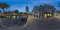 a 360 - view photo of a red car and a road by the canal in a town