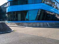 a skate park that is near a blue building with windows on it and skateboard ramps in the foreground