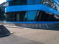 a skate park that is near a blue building with windows on it and skateboard ramps in the foreground