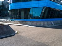 a skate park that is near a blue building with windows on it and skateboard ramps in the foreground