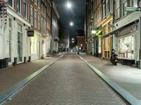 a narrow brick paved city street in the evening, with a man sitting on a motorcycle parked next to it