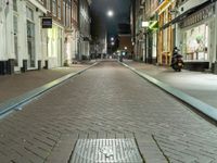 a narrow brick paved city street in the evening, with a man sitting on a motorcycle parked next to it