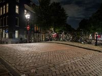 bicycles and buildings on the street at night in a town of amsterdam, with traffic