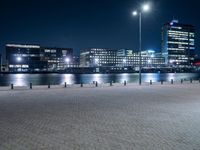 an empty brick pathway beside the water at night with lights shining on it's sides