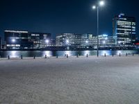 an empty brick pathway beside the water at night with lights shining on it's sides