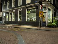 a view of a street corner at night with many shops with windows and no parking sign