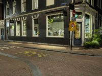 a view of a street corner at night with many shops with windows and no parking sign