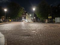 night scene of city block with cobblestone pathway and multiple light posts and lights