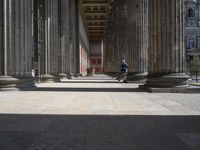 large columns and a stone vase in an open space with windows in the background,