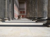 large columns and a stone vase in an open space with windows in the background,