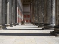 large columns and a stone vase in an open space with windows in the background,