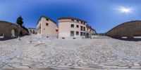 a fish eye photo shows the front entrance to an ancient city with stone buildings and cobblestones in a street