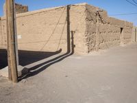 a lone telephone pole is casting a shadow on the stone wall of an adobe hut