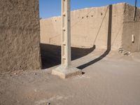 a lone telephone pole is casting a shadow on the stone wall of an adobe hut