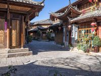 a small paved courtyard with wooden doors and wooden pillars surrounding the area is lined with tall, ornate brick and painted architecture