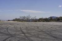 a view along a dirt road of an empty field and mountains in the distance of the scene