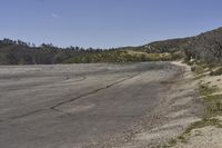 a view along a dirt road of an empty field and mountains in the distance of the scene