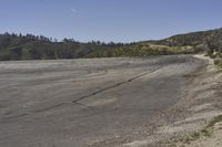 a view along a dirt road of an empty field and mountains in the distance of the scene