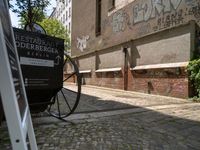 an antique cart on the side of a narrow street near a building and graffiti covered wall