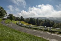 a road with white fences leads down to a green mountain range and there are trees in the background