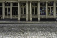 the front entrance to an old building with pillars and columns on it on a brick street