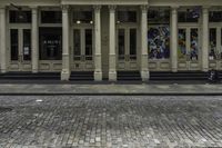 the front entrance to an old building with pillars and columns on it on a brick street