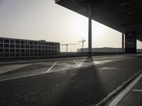 the sun is setting in the back of the building while the road and tracks are empty