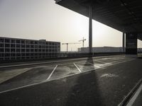 the sun is setting in the back of the building while the road and tracks are empty