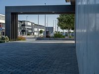 the large black gate is opened on an empty street near buildings with trees, bushes and a bench in it