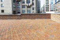 red brick floor with two building in the background from top of a roof and on the ground is a brick wall
