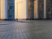 a person sits on top of a stone floor next to a street with pillars in the background