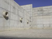 a concrete wall and round windows with circular holes on it in front of it and a blue sky