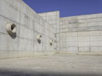 a concrete wall and round windows with circular holes on it in front of it and a blue sky