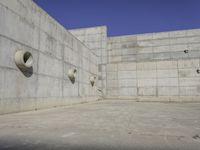 a concrete wall and round windows with circular holes on it in front of it and a blue sky