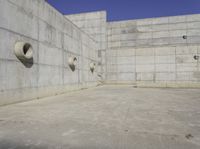 a concrete wall and round windows with circular holes on it in front of it and a blue sky