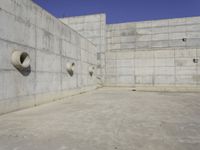 a concrete wall and round windows with circular holes on it in front of it and a blue sky